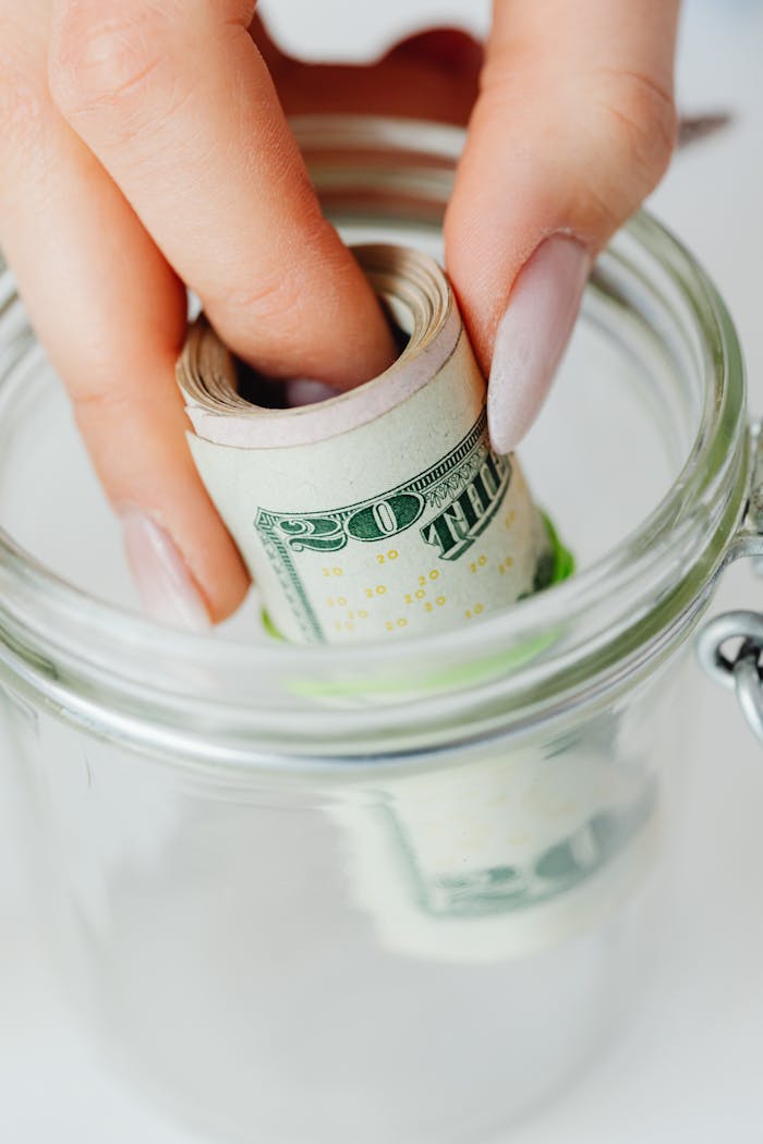The Art of Drawing Readers In: Your attractive post title goes here Hand placing rolled US dollars into a glass jar, representing savings and financial planning.